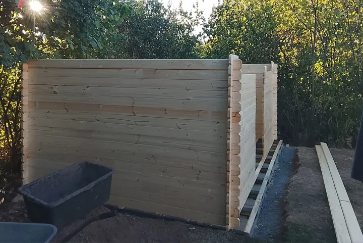 Aufgerichtete Blockbohlenwände des Gartenhauses auf dem Lagerholz